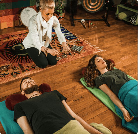 A woman guides two people in a meditation session indoors.