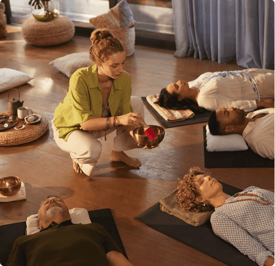 A woman leads a meditation session with participants lying on mats.